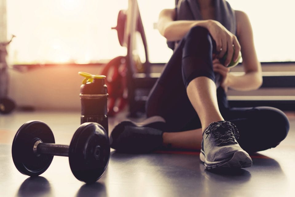 woman sitting on floor after workout with dumb bell and water bottle