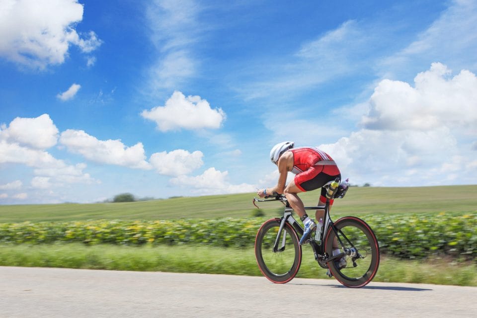 man cycling on road bike with blue sky and grass behind him