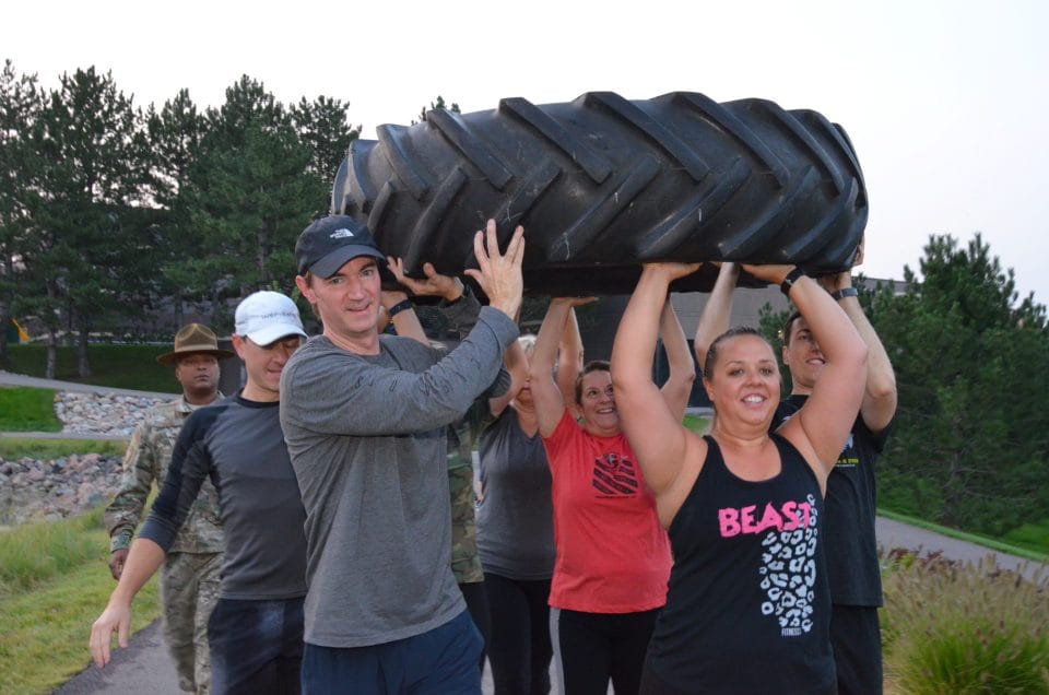 people lifting tire up with teamwork outside in boot camp class at greenwood village park