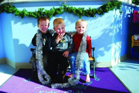 kids sitting on small bench and smiling with holiday decorations