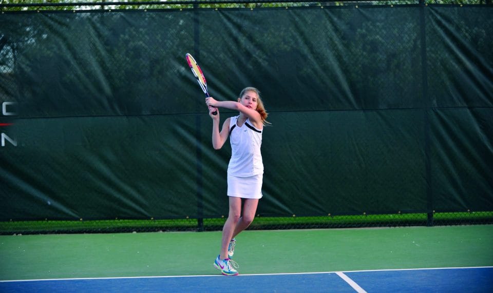 girl in white dress playing tennis on outdoor court