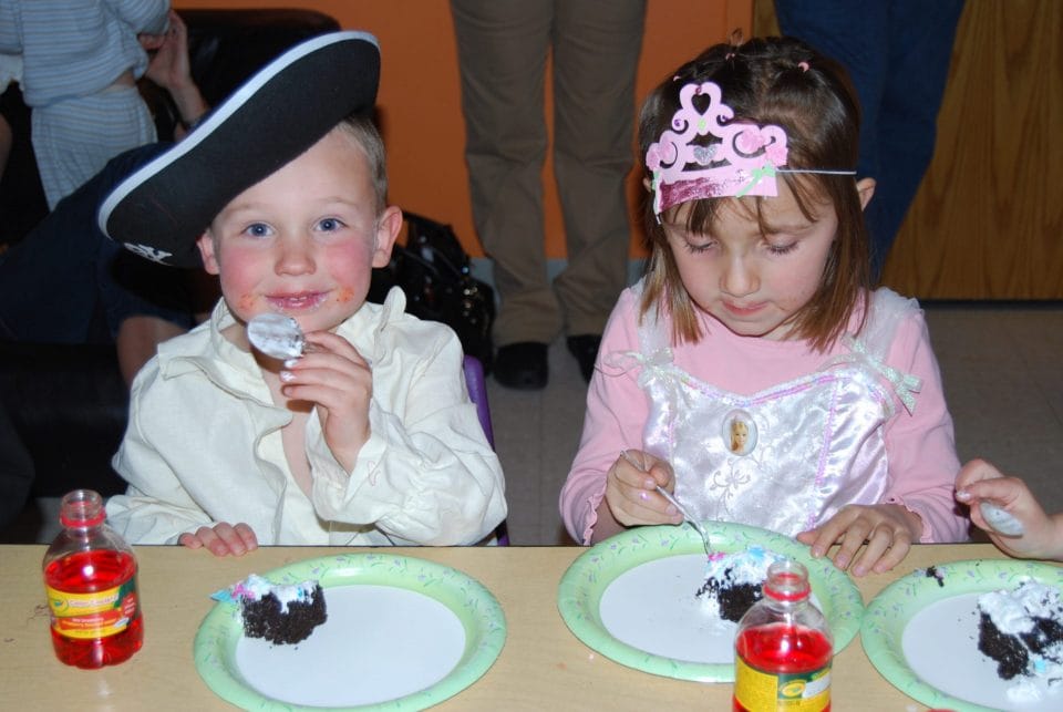 kids dressed as a pirate and a princess eating cake during a birthday party in kids' club