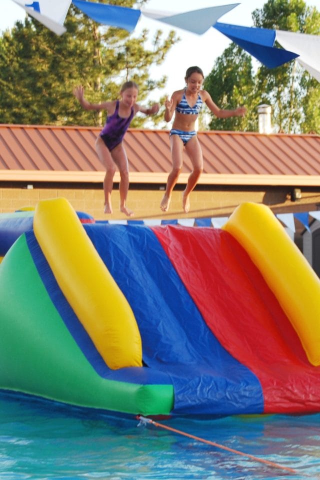 two kids jumping onto an inflatable pool slide