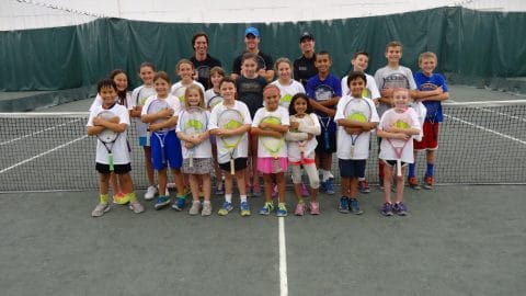 kids and coaches in a group photo for junior tennis camp smiling with tennis racquets