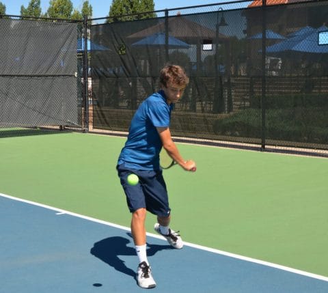 teen hitting tennis ball with racquet and wearing blue on club greenwood outdoor tennis court