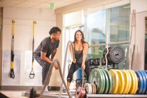 woman working with personal trainer on battle ropes