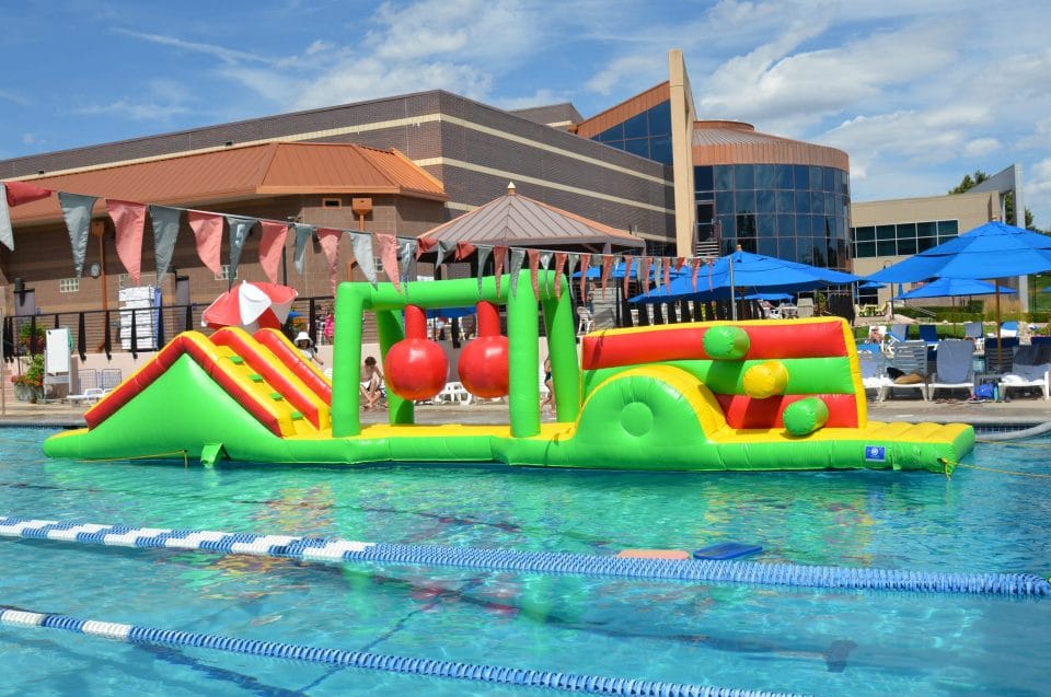 huge red, green, and yellow pool float in club greenwood outdoor pool in front of the club greenwood facility