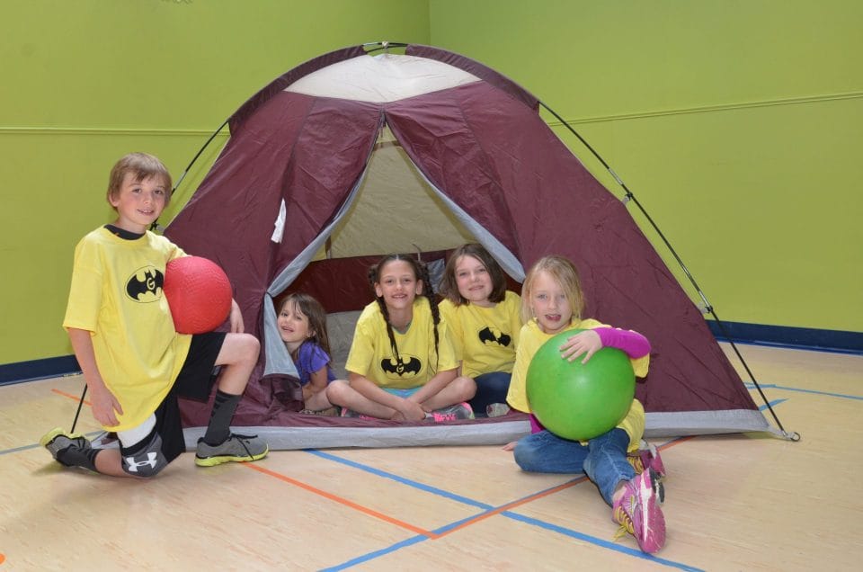 kids in yellow shirts sitting inside of and next to a tent in youth activities club for summer day camp