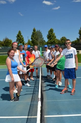 teens standing with tennis racquet next to tennis net and smiling