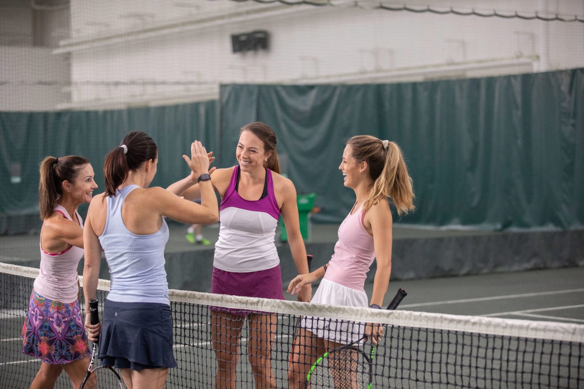 women high five at a tennis net after playing a match on Club Greenwood indoor clay courts