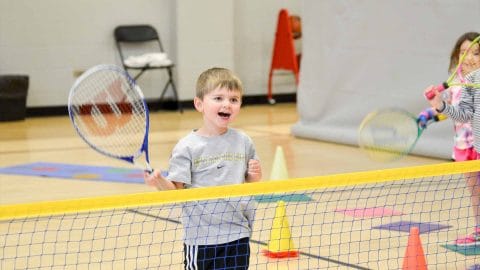 little boy playing tennis in a gymnasium