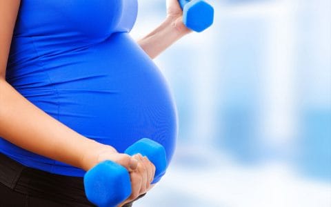 pregnant woman in blue shirt working out and lifting blue dumb bells