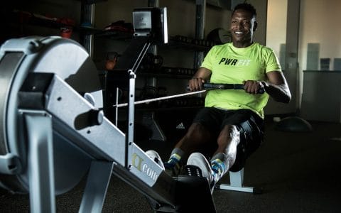 Personal Trainer Brandon Smith in bright green shirt on a rowing machine in dark room