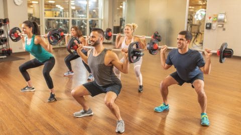 people working out in a group fitness class squatting with barbells