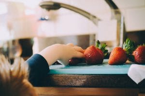 small kid reaching for strawberries on a countertop