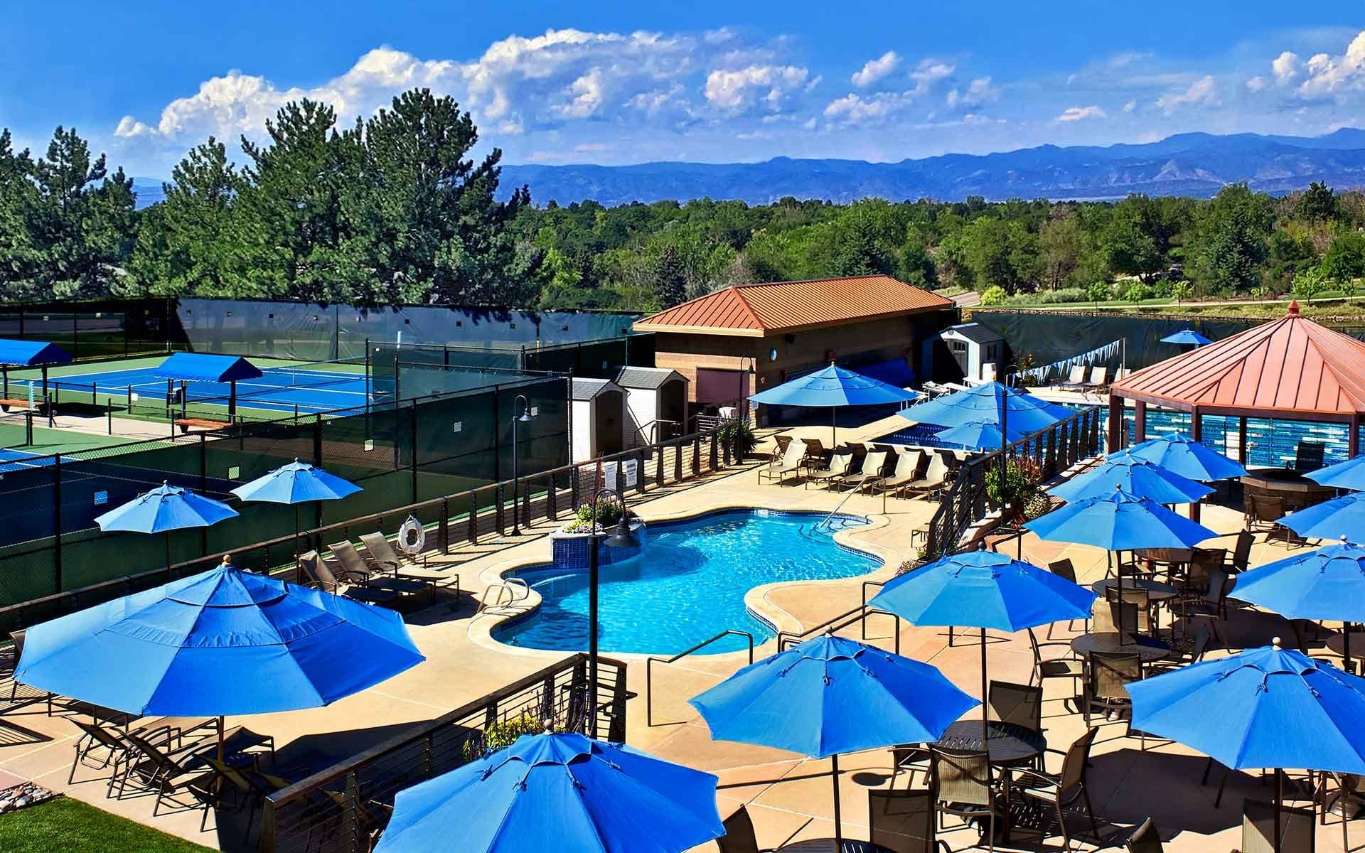 outdoor pool and tennis courts with umbrellas and mountains in the background