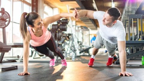 man and woman doing a high plank workout and high fiving at a gym