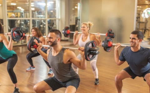 People squatting with bar bells and working out a Club Greenwood