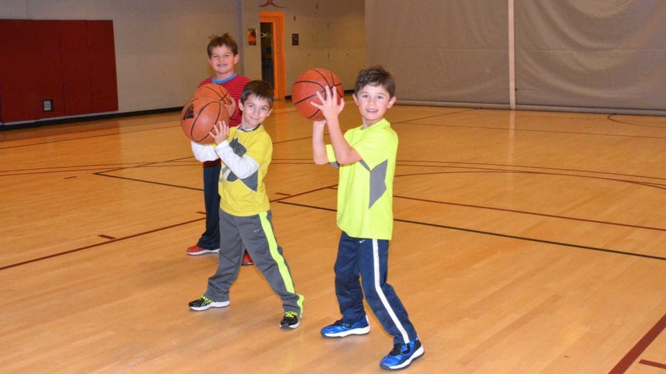 three kids playing basketball at Club Greenwood and smiling