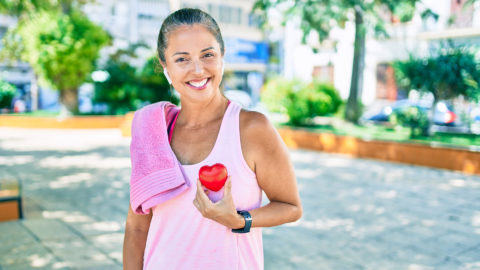 Woman holding plastic heart with workout towel on her shoulder