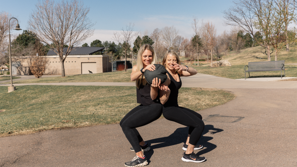 two women using sand bells in the outdoors