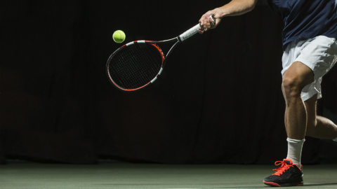 male playing tennis under the lights