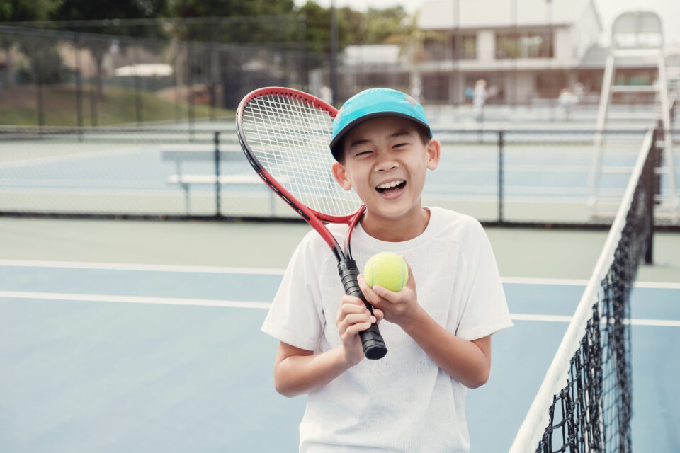 Youth smiling and holding tennis ball and tennis racquet on tennis court
