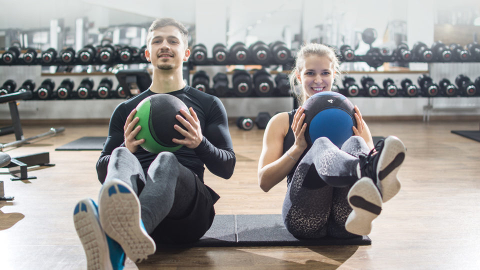 Fit couple doing abdominal exercise with fitness balls at gym.