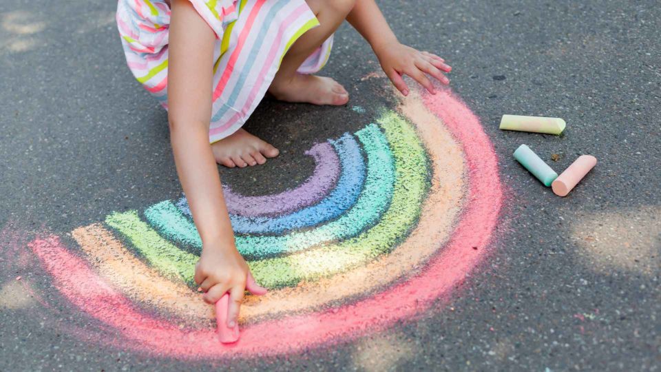 young girl drawing a rainbow on the ground with sidewalk chalk