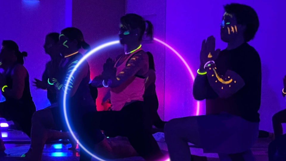 People doing yoga in a black light room with neon lights in a party atmosphere