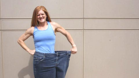 club greenwood personal trainer Kim Galbreath shows her weightloss by standing in one paint leg of her old jeans in front of a beige wall