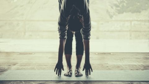 woman doing yoga on a yoga mat standing in a forward fold touching the floor