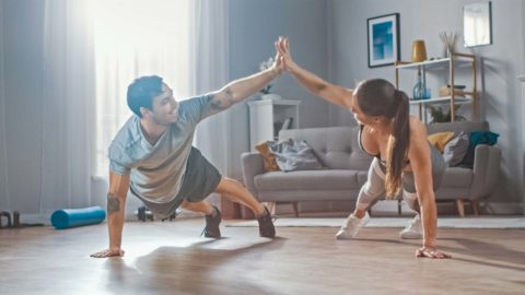 man and woman working out at home, doing a plank and high fiving