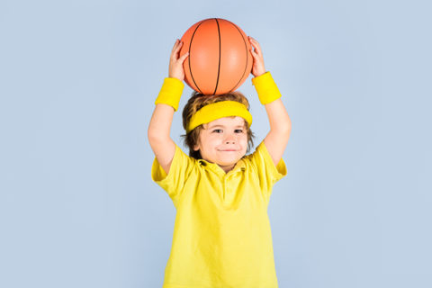 cute little boy in a yellow shirt holding a basketball over his head