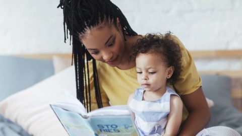 mom wearing a yellow shirt reading a book to her toddler