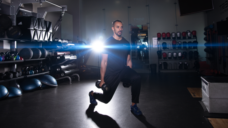 male personal trainer performing a dumbbell lunge exercise in a studio