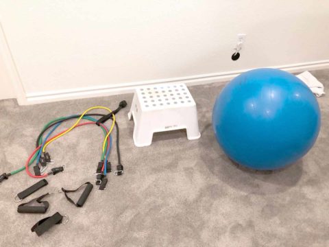 workout bands, step, and stability ball sitting on grey carpet