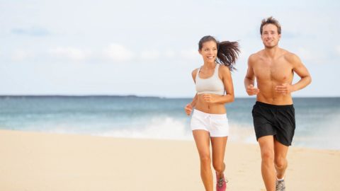 man and woman running together on the beach smiling