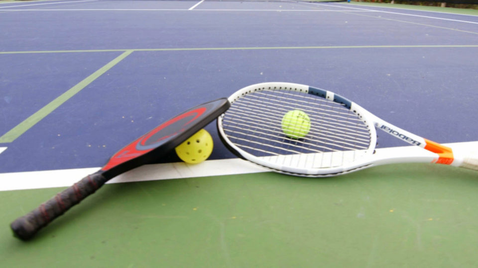 Pickleball Racquet and ball and Tennis Racquet and ball laying on court