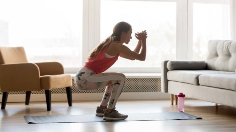 woman working out at home doing a squat on an exercise mat