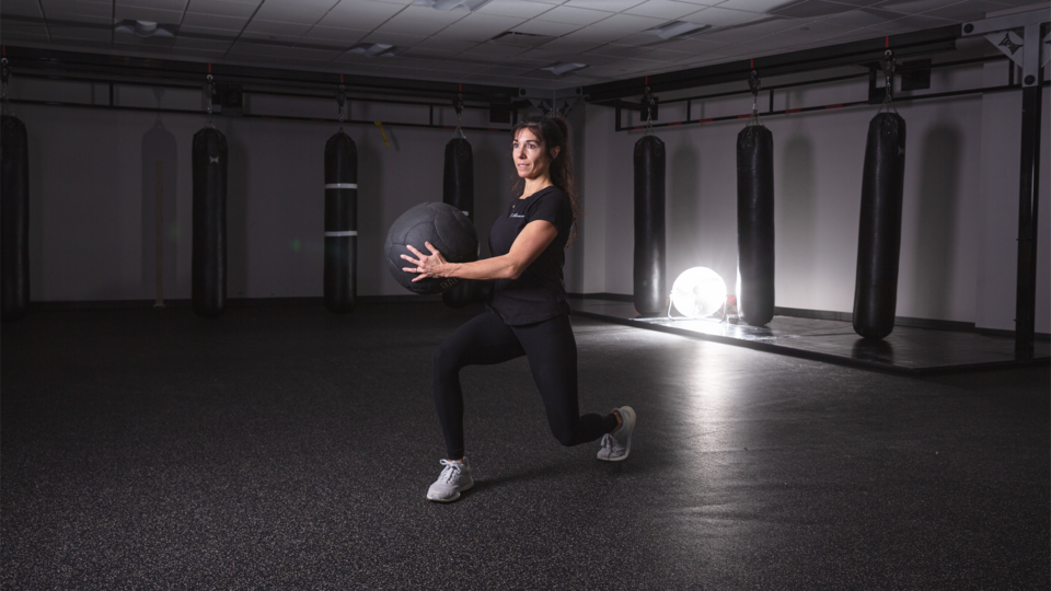 female trainer performing a reverse lunge with medicine ball