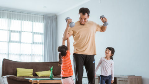 Dad working out with dumbells while kids hang on him