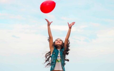 girl with long hair playing with a red balloon outside