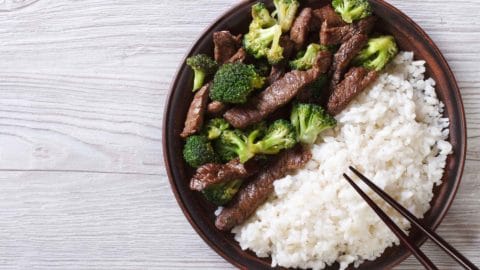 plate of beef, broccoli, and rice with chopsticks on a white table