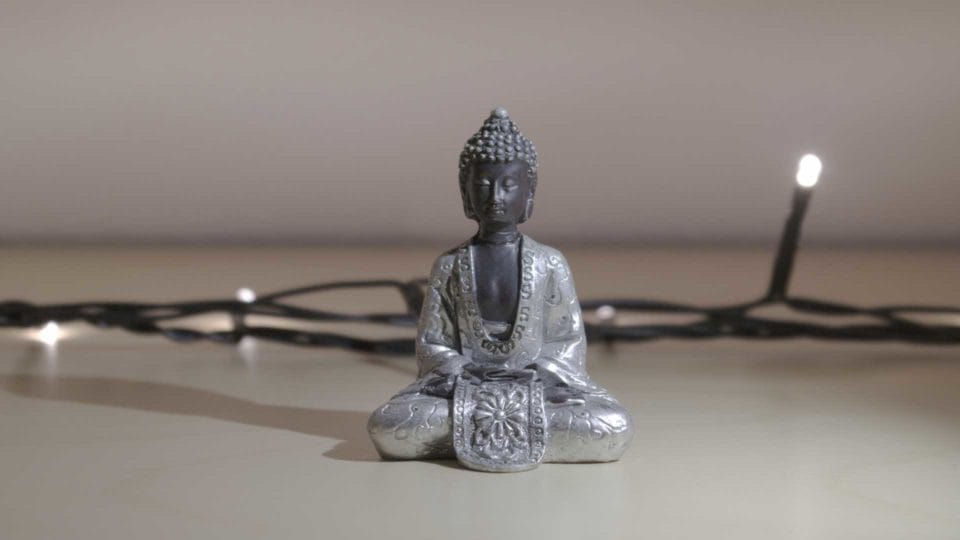 buddha statue sitting in a gray room in front of twinkle lights
