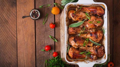 chicken in pan sitting on a wooden table with tomatoes and herbs