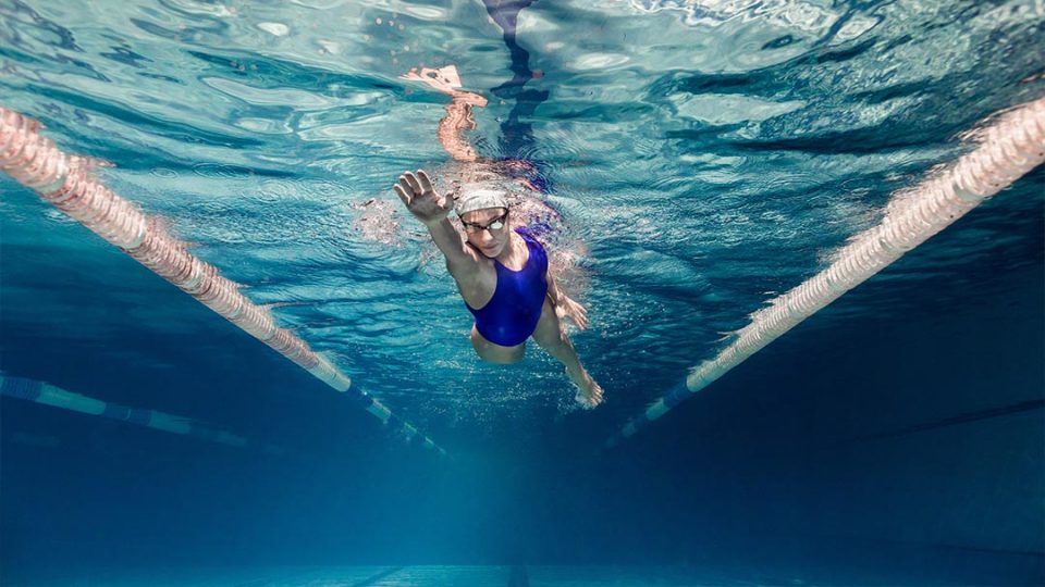 woman swimming under water wearing goggles and a blue swim suit