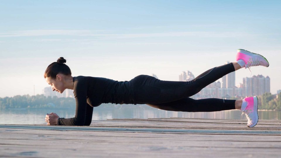 woman wearing black doing a forearm plank outside in a park during daytime