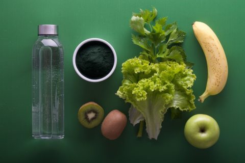 lettuce, kiwi, apples, banana and water laying on a green table