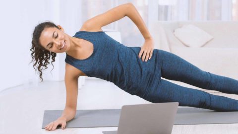 woman working out at home with a lap top wearing a blue workout outfit